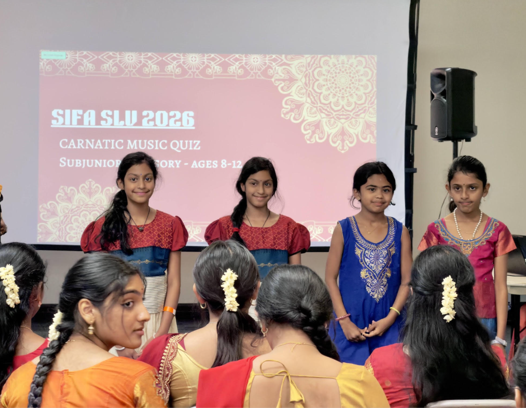 Four young quiz contestants standing in front of a screen reading SIFA SLV 2026 Carnatic Music Quiz